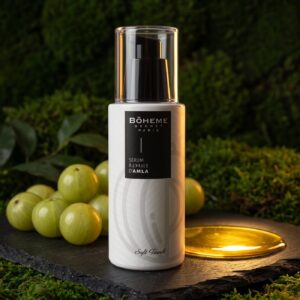 Flacon pompe du sérum capillaire à l'huile d'amla Bôheme Secret Paris sur de l'ardoise, entouré de baies d'amla fraîches et d'une coupelle d'huile dorée